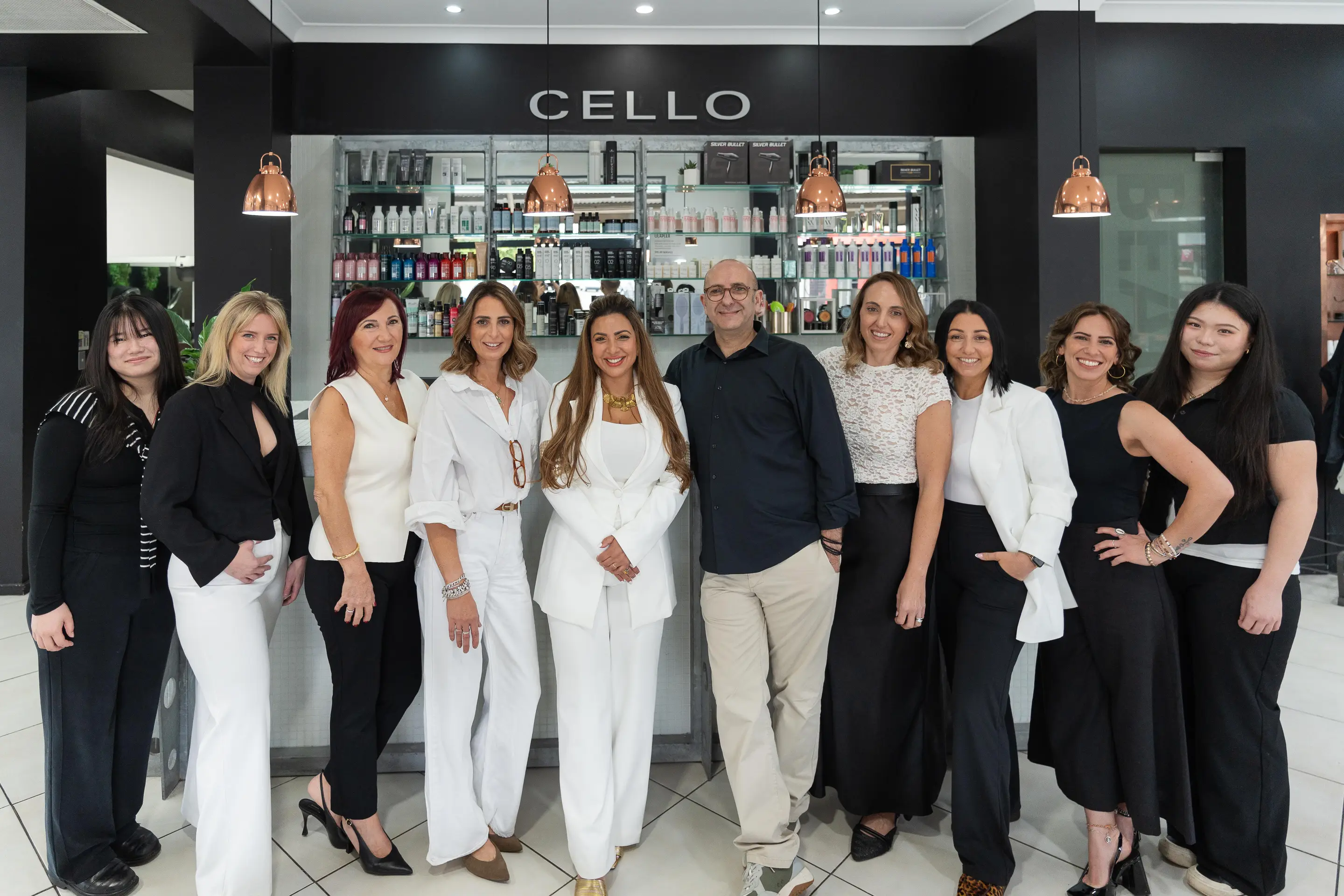 The Cello Hairdressers team, ten of them, standing together in front of the reception desk under the CELLO sign in Five Dock.
