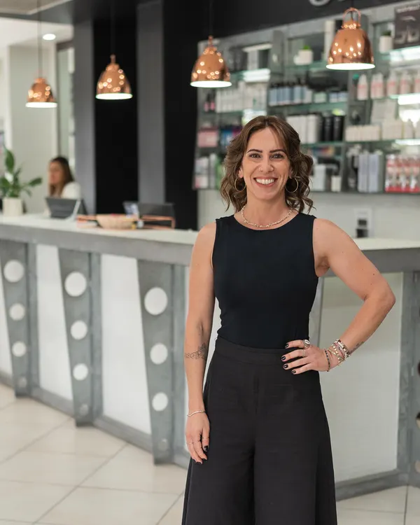 Claudia, emerging stylist at Cello Hairdressers, with a hand on her hip in front of the reception desk.
