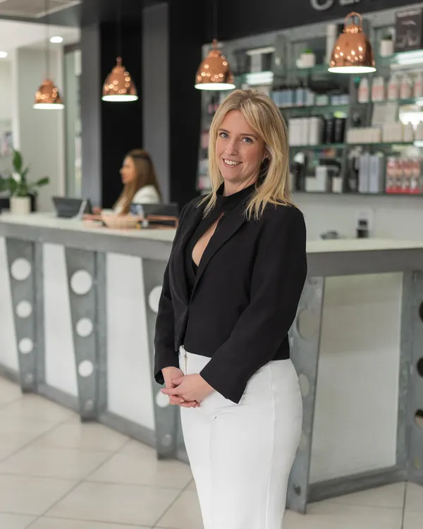 Katie, senior stylist at Cello Hairdressers, in a black blazer in front of the reception desk.