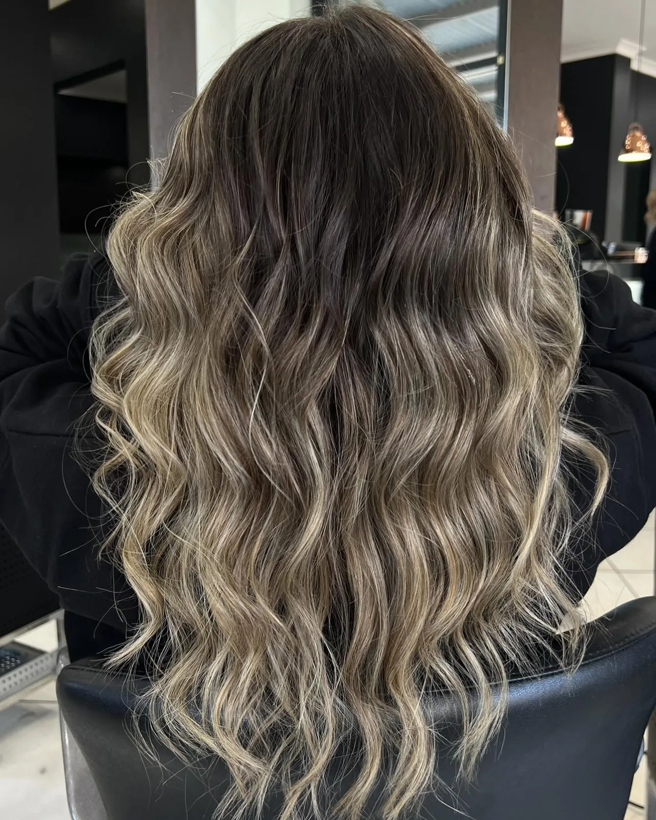 Long hair with a lived-in balayage graduating from a dark root to sandy ends, waved out on the salon floor at Cello Hairdressers.